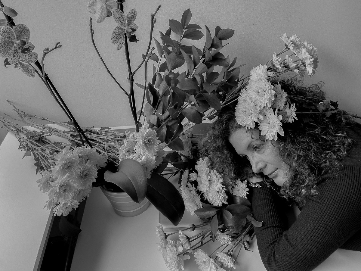 Black and white image of a person surrounded by flower arrangements.