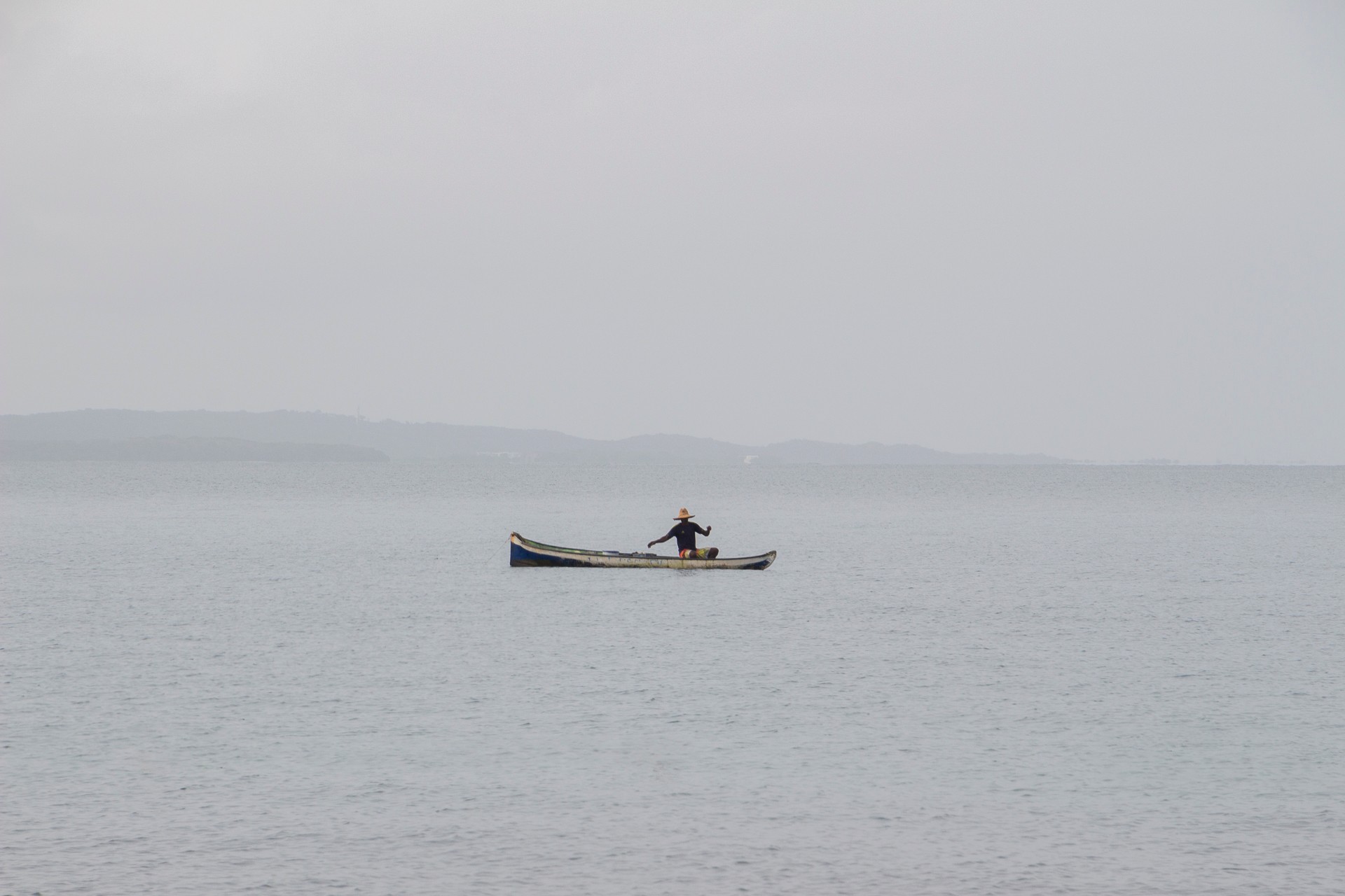 Image of a small boat floating on calm water with a foggy horizon.